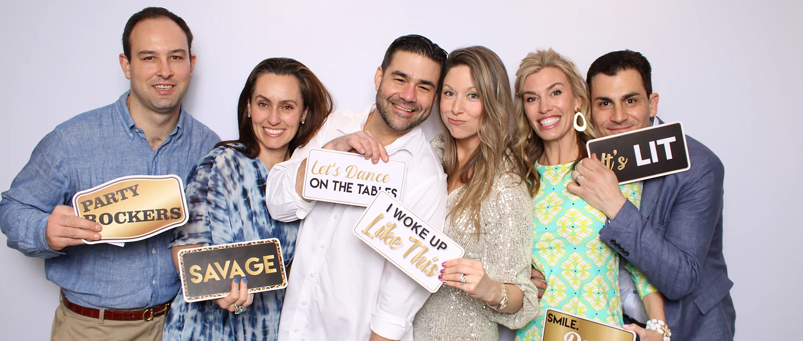 Six guests laughing together while holding handheld photo booth prop signs