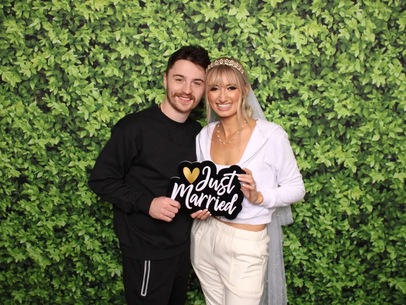 Just married couple posing with prop signs in front of a leaf wall backdrop