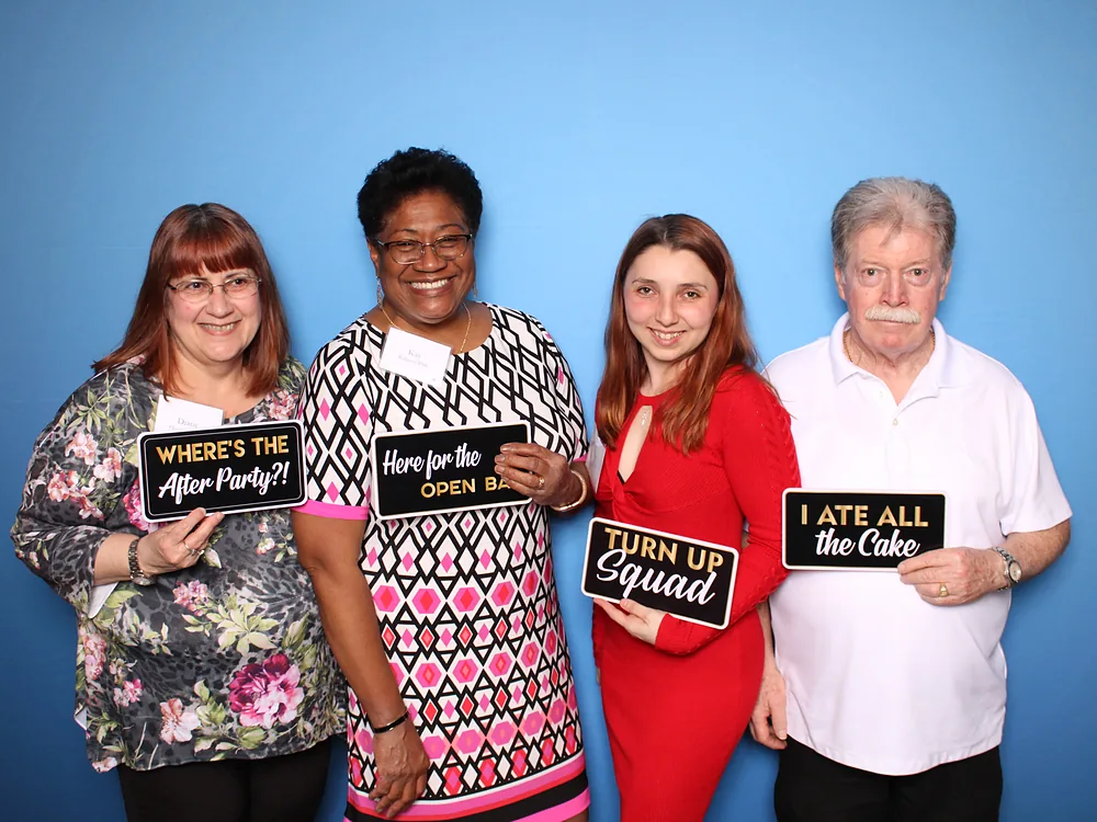 Coworkers celebrating with photo booth prop signs against a blue backdrop