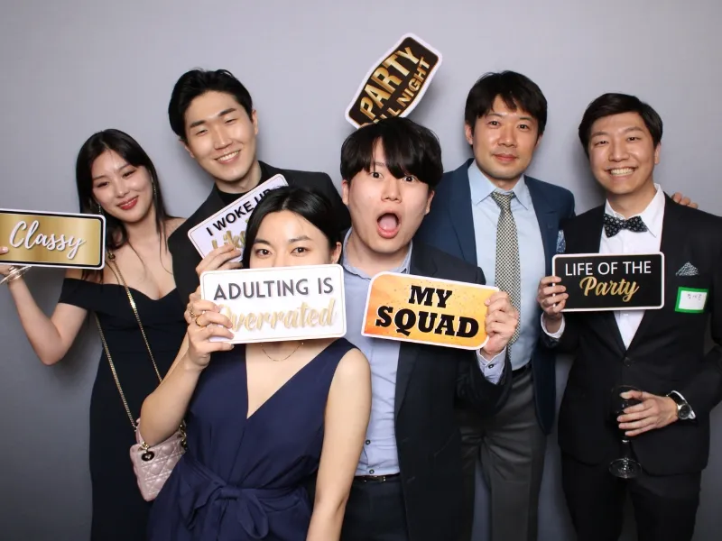 Large group of students posing with photo booth prop signs against a gray backdrop