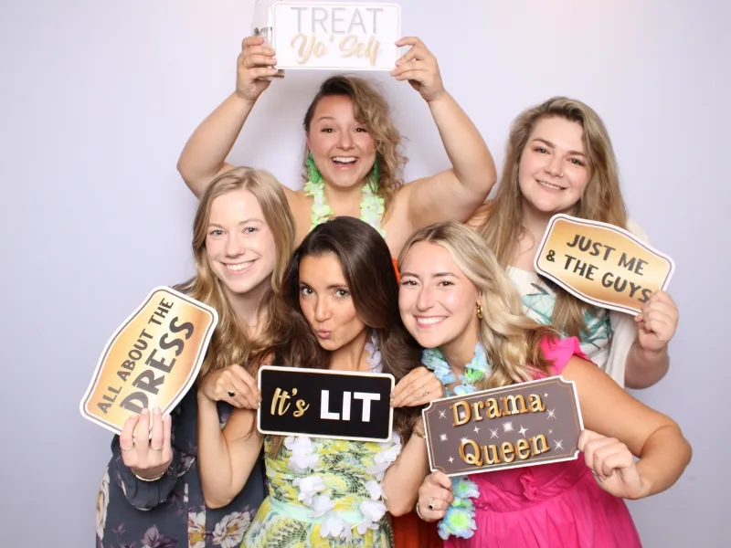Large group of women posing with photo booth prop signs against a white backdrop