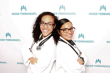 2 Female doctors pose back to back in front of a step and repeat back ground