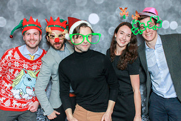 Employees pose with silly props at the photobooth in front of a sparkle back ground