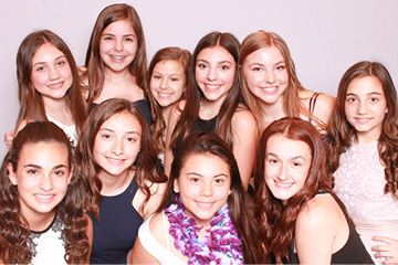 A large group of young girls pose together with props at a Bat Mitzvah photo booth
