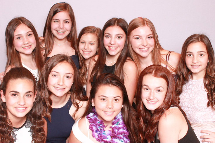 A large group of young girls pose together with props at a Bat Mitzvah photo booth