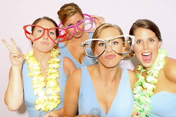 Group of Bridesmaids dressed in blue pose with colorful wedding photobooth props