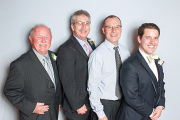 Four family men pose together formally at a wedding photo booth for a group photo